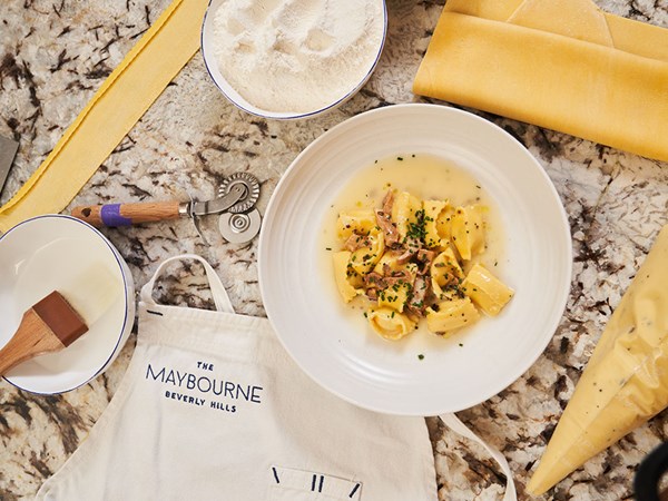 Bowl of freshly made pasta on marble work top with fresh dough and pasta cutting tools placed around