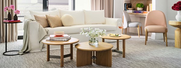 White sofa with matching cushions and throw in living room with brown coffee table in the middle and a desk and pink chair on the right